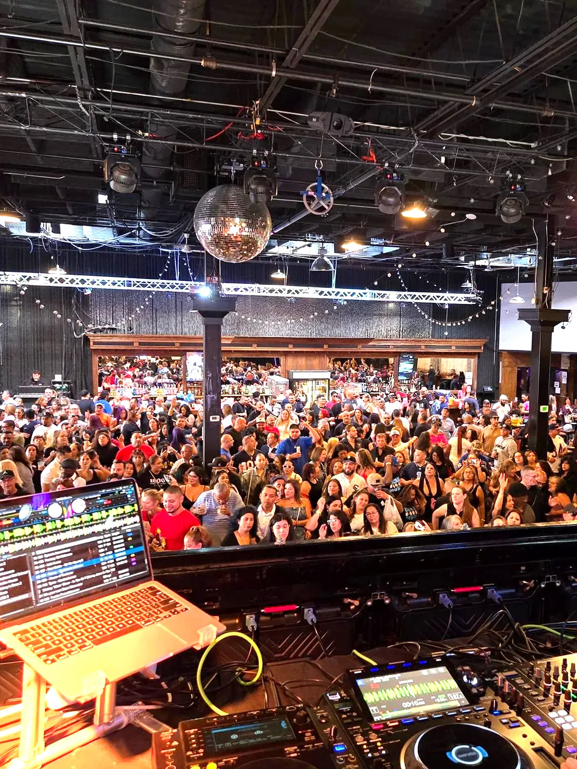 Scott Silz behind the DJ booth overlooking a packed nightclub crowd with disco ball