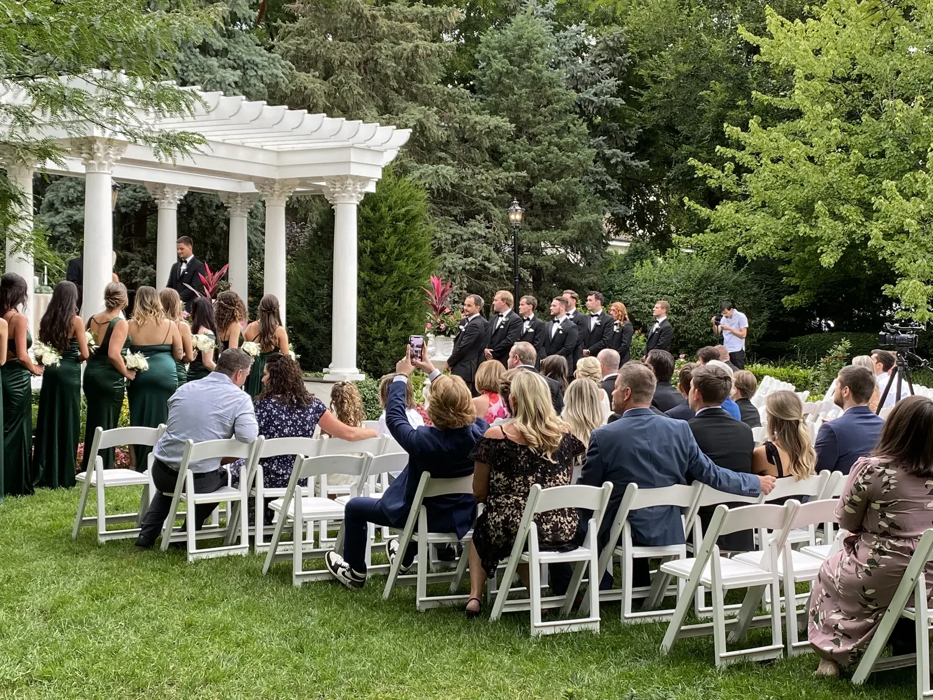 Outdoor wedding ceremony under a gazebo with guests seated in the sunshine