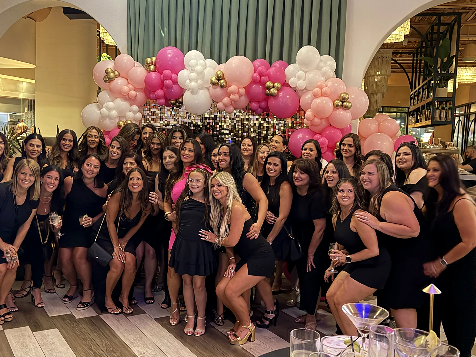 Group of women celebrating a birthday with pink and white balloon arch at an upscale venue