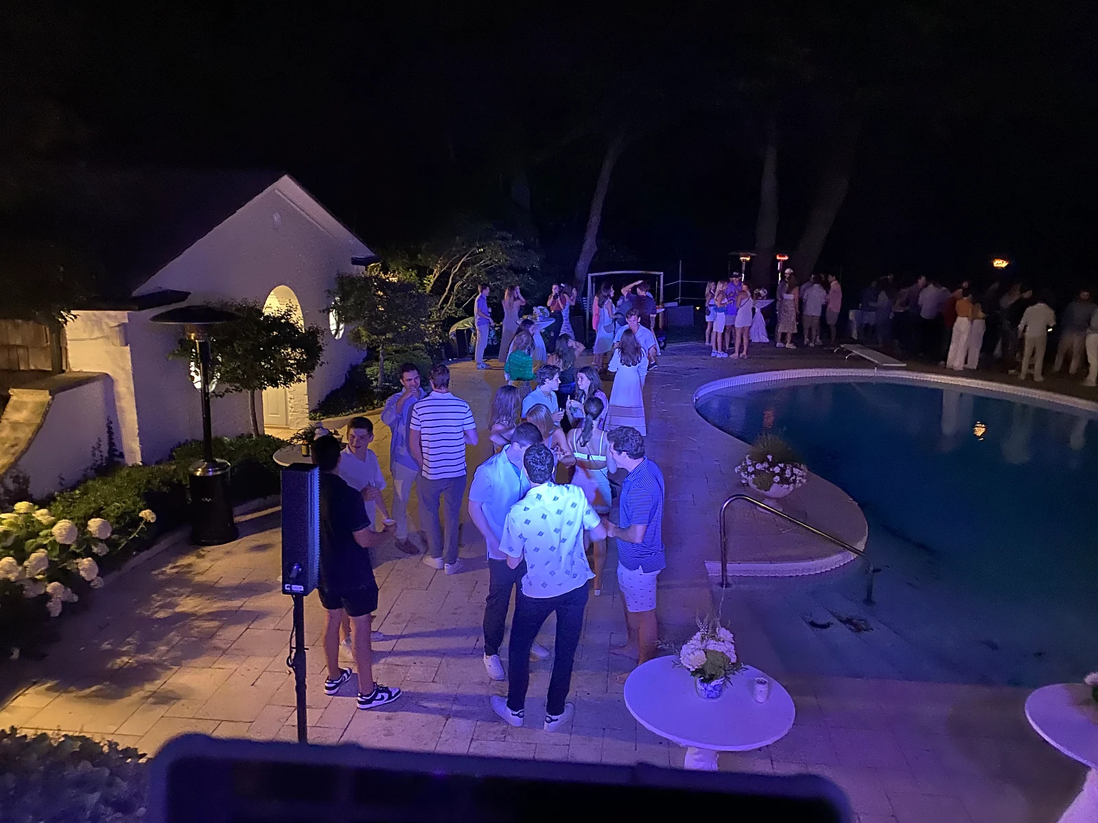 Guests socializing by the pool at an evening private party with blue uplighting