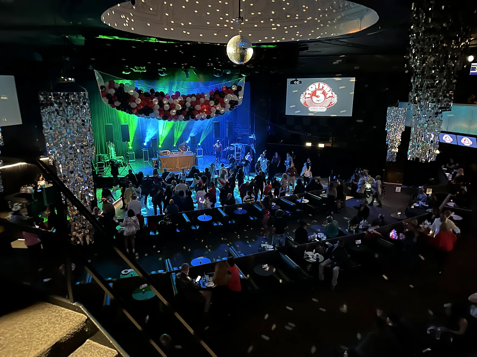Hot Mix 5 logo on screen at a large nightclub venue with balloon arch and stage lighting