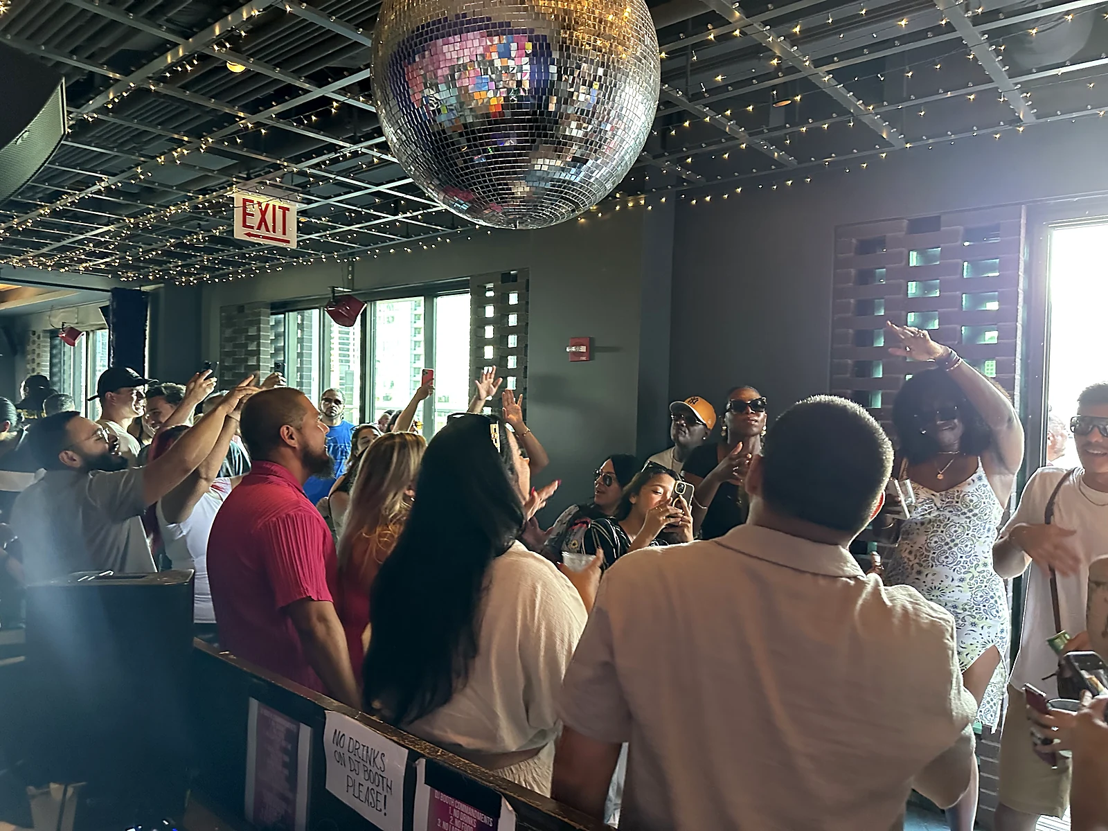 Packed crowd dancing under a disco ball with hands raised at a rooftop party