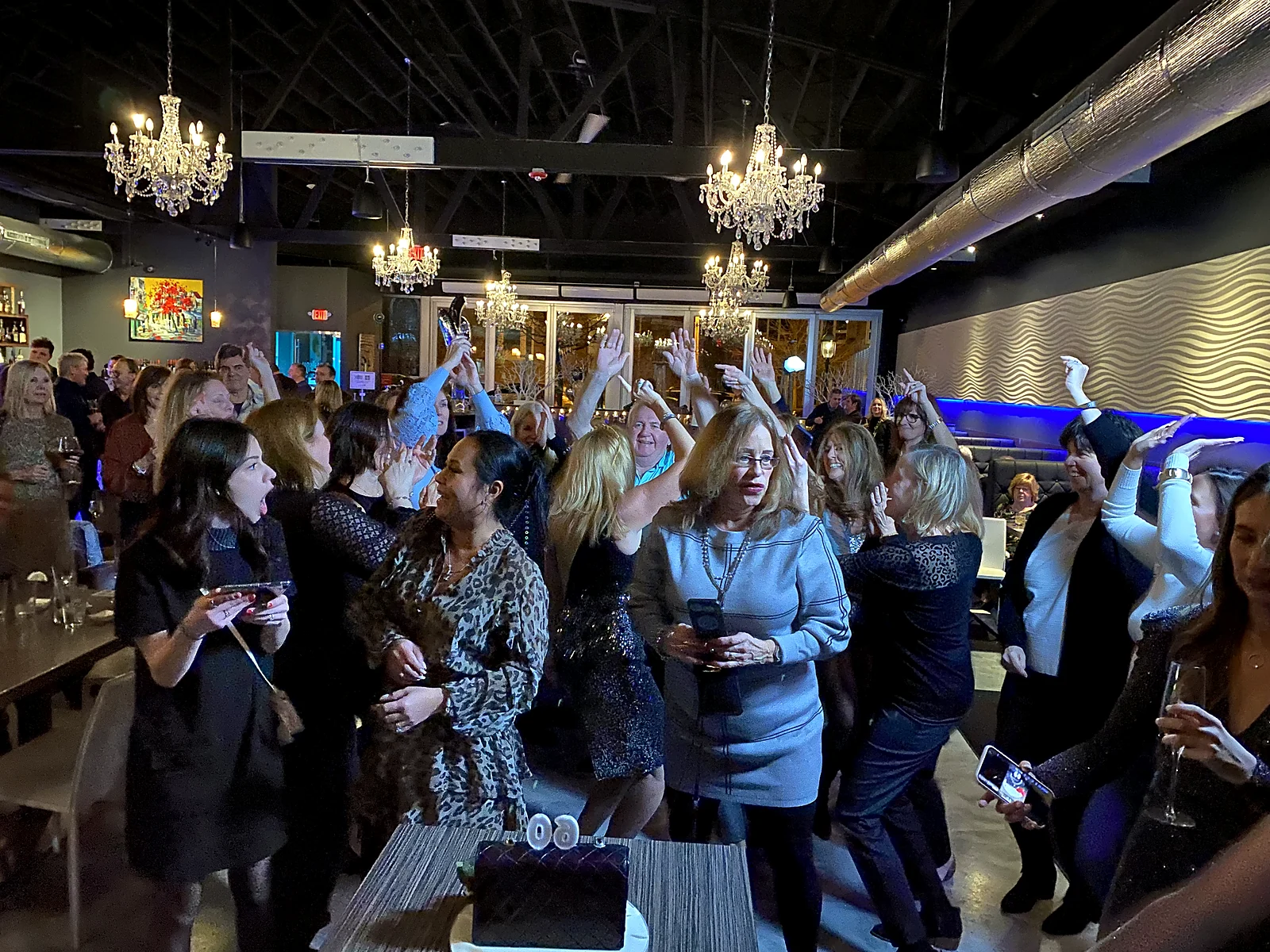 Guests with hands raised dancing under crystal chandeliers at an elegant private celebration