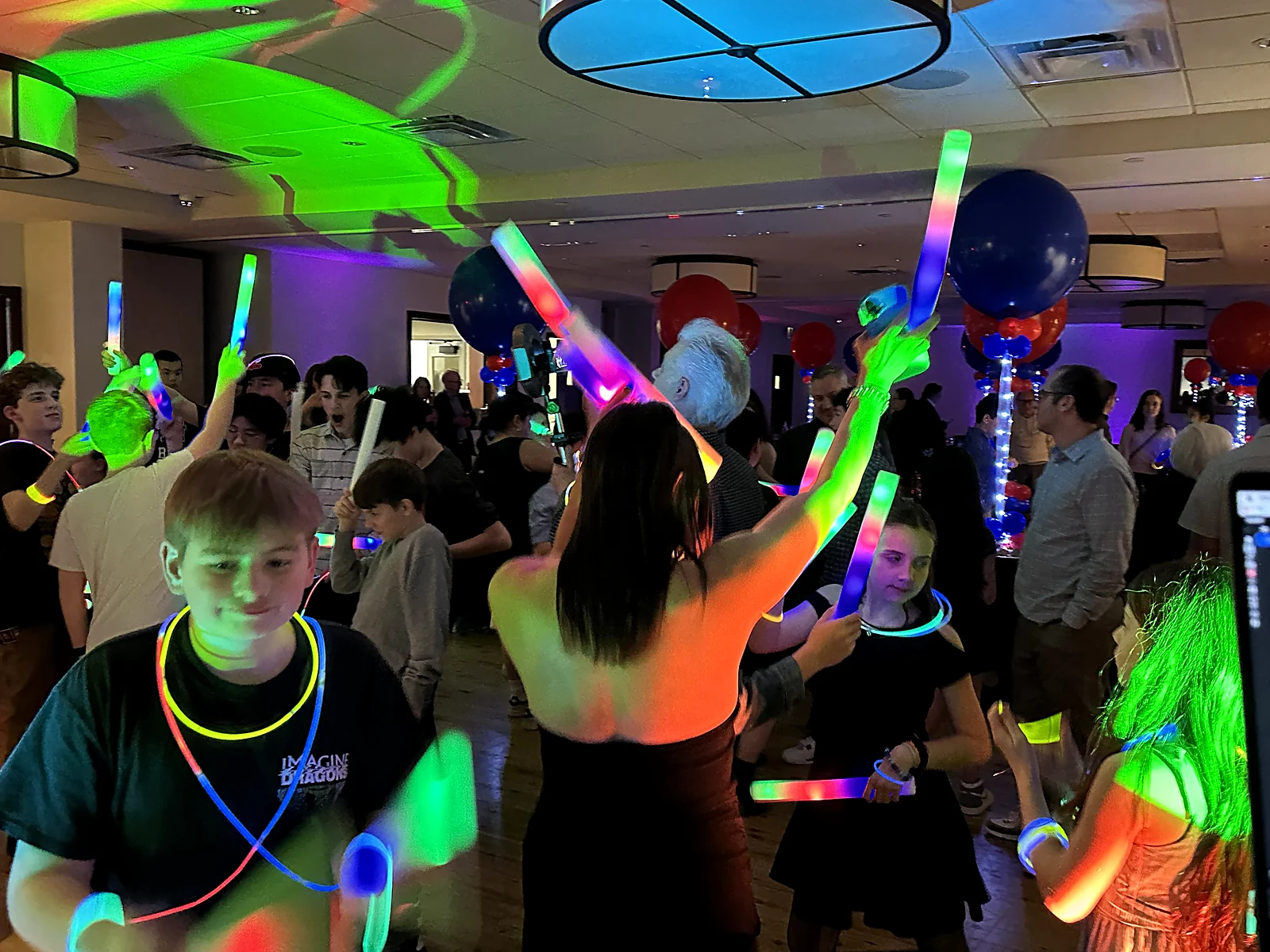 Kids and families with hands raised and glow sticks on a packed dance floor