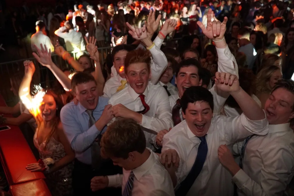 Students cheering with hands raised on a packed prom dance floor