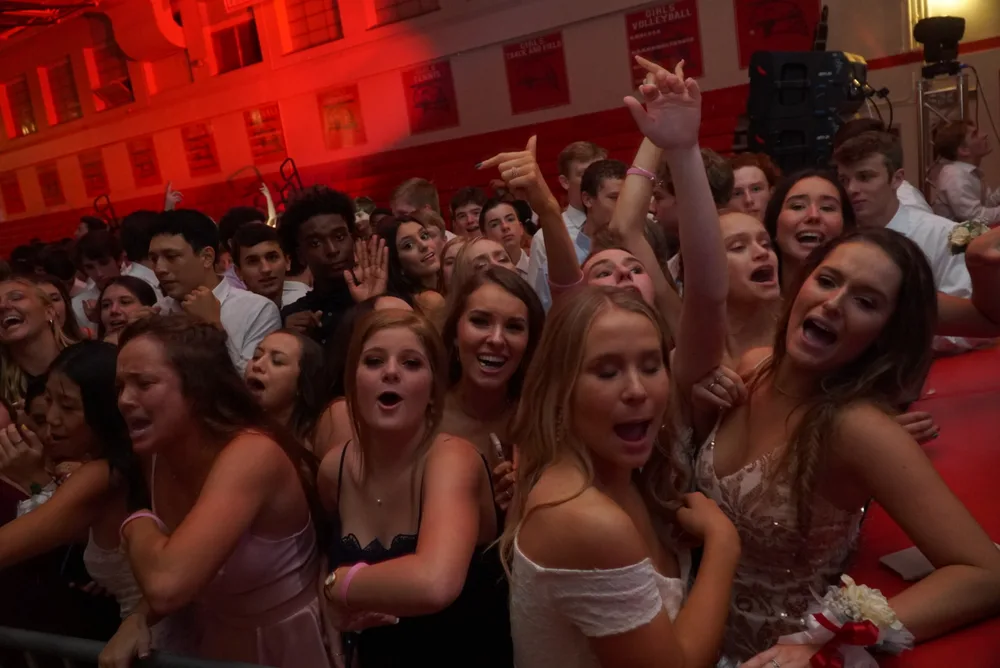 Crowd of students singing along at a homecoming dance with red uplighting