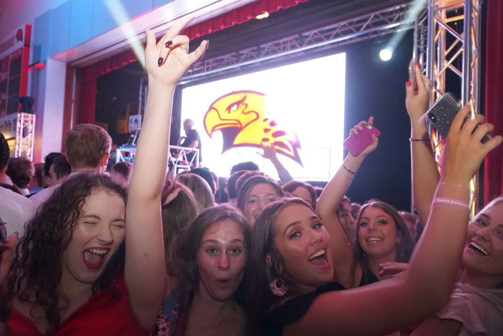 Students taking selfies and cheering in front of the school mascot screen